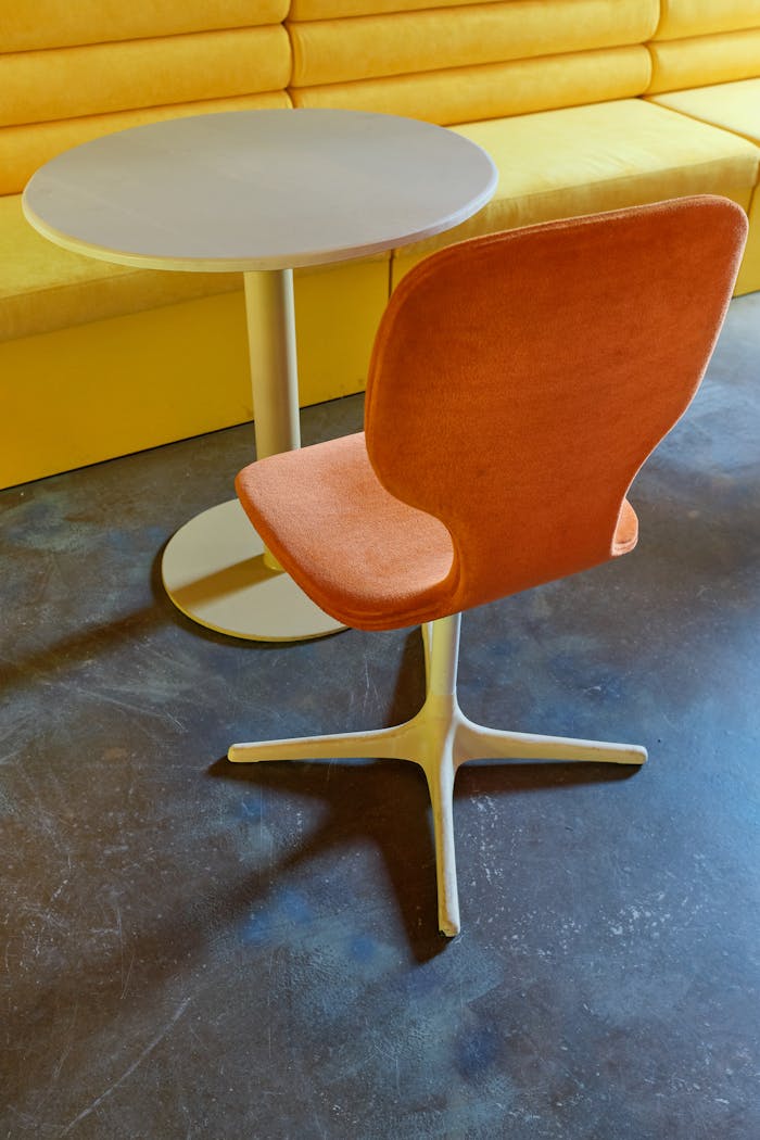 Productos y Servicios Contemporary orange chair with round table against yellow bench, showcasing modern interior décor.
